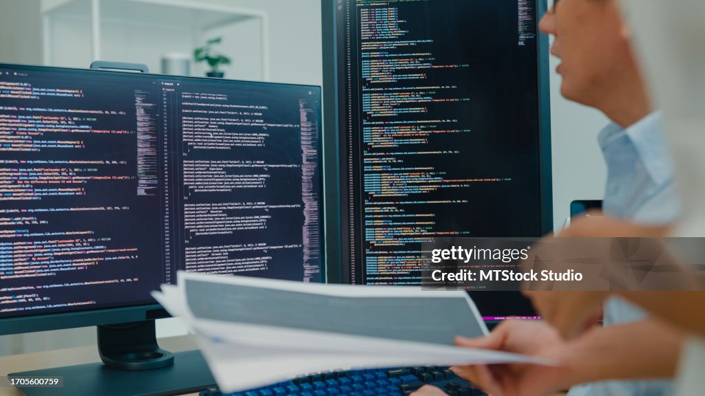 Closeup group of Asian people software developers using computer to write code sitting at desk with multiple screens at office. Programmer development.