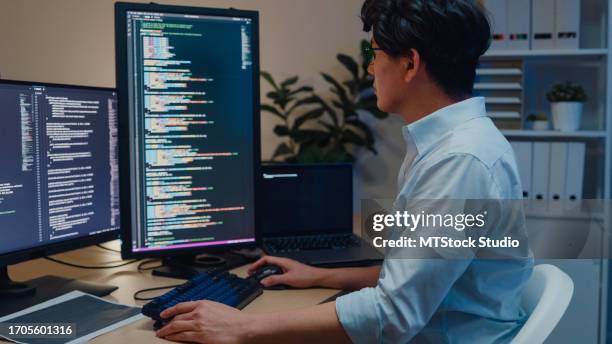 junge asiatische softwareentwickler, die computer verwenden, um code zu schreiben, sitzen am schreibtisch mit mehreren bildschirmen und arbeiten nachts im büro. entwicklung von programmierern. - javascript stock-fotos und bilder