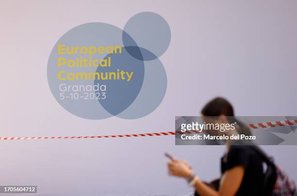 Woman holds a smart phone in front of a European Political Community meeting logo on October 4, 2023 in Granada, Spain. Heads of state or government...