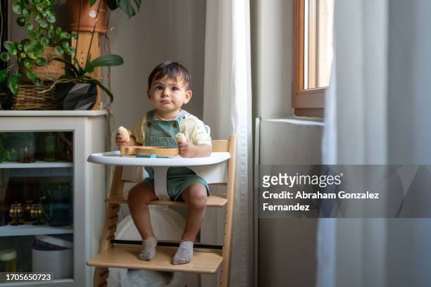 cute kid eating banana in a baby high chair - newfamily stock pictures, royalty-free photos & images