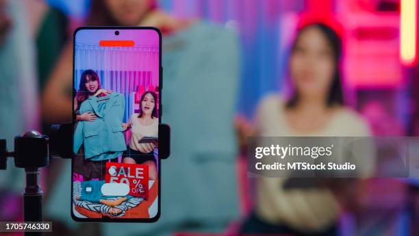 closeup of young asian women live streaming on phone show new collection fashion clothes to customer in shop at night. sme small business e-commerce. - media buying stock pictures, royalty-free photos & images