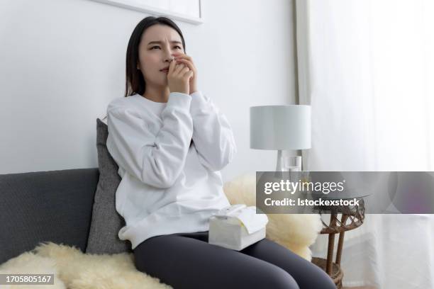 young pretty asian girl sitting on a cozy sofa in the living room and watching tv. - film screening room stock pictures, royalty-free photos & images