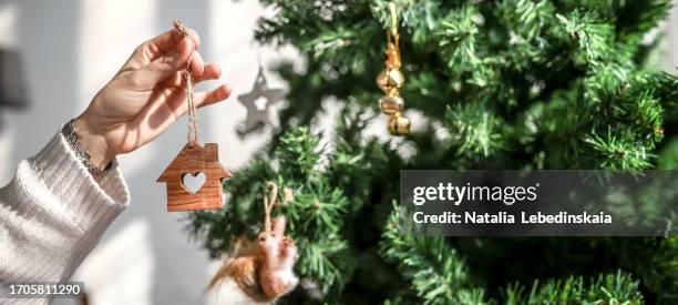 wooden toy house with heart shape window in woman's hand - decoration of christmas tree and dreams of home, banner and copy space - homeowners decorate their houses for christmas stockfoto's en -beelden