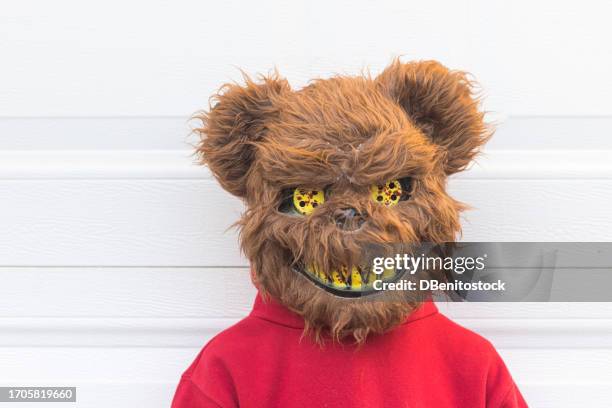 young person in a halloween costume wearing a killer bear mask over a white garage door. concept of day of the dead, fear, terror, halloween, scare and trick or treat. - malvagità foto e immagini stock