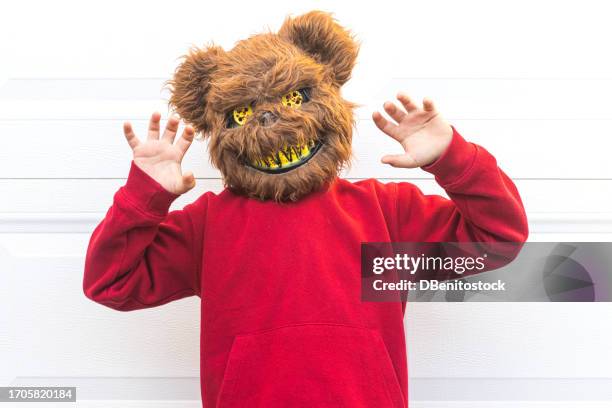 young person in a halloween costume wearing a killer bear mask, scaring with his hands, over a white garage door. concept of day of the dead, fear, terror, halloween, scare and trick or treat. - colors against violence in madrid stockfoto's en -beelden