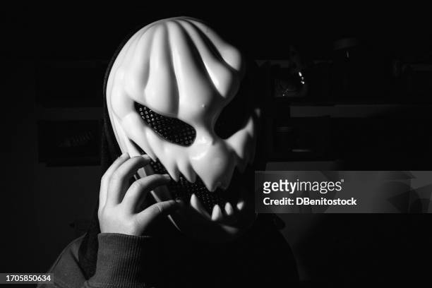 black and white photo of person wearing halloween pumpkin mask on low key and dark background, clutching his face madly. concept of day of the dead, fear, terror, halloween, scare and trick or treat. - ugly lips stock pictures, royalty-free photos & images