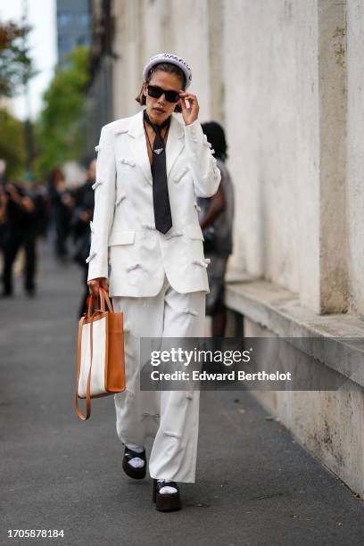 Guest wears a Maison Margiela headband, a piercing, a Prada black tie, a two-tone bag, a white pantsuit decorated with white sequined bows, black...