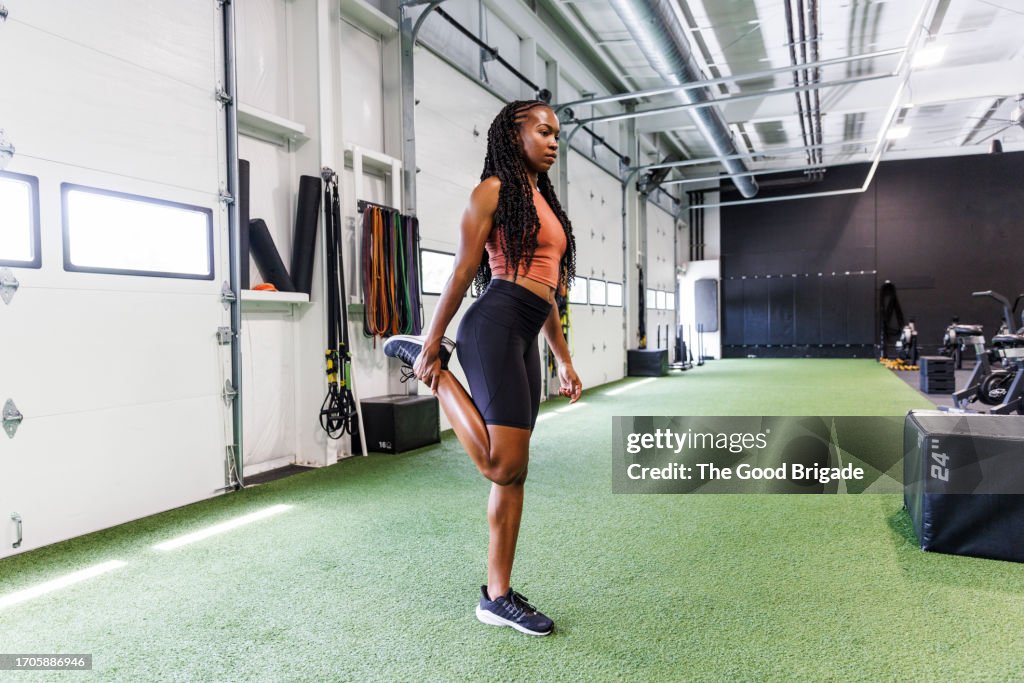 Full length of young woman stretching leg while exercising at gym