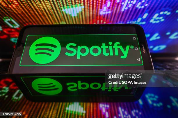 In this photo illustration, Spotify logo seen displayed on a smartphone with stock market percentages in the background.