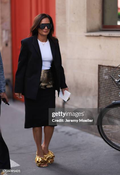 Guest is seen outside The Row show wearing big black Loewe sunnies, black blazer, white tank top, black midi skirt with golden brush details and...