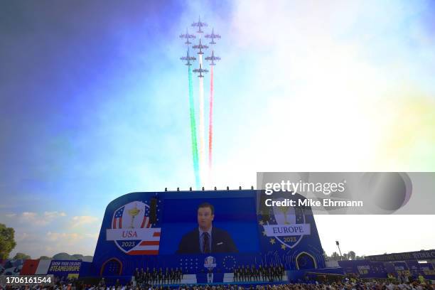 The Frecce Tricolori perform a display over the crowd and stage as Zach Johnson, Captain of Team United States talks during the opening ceremony for...