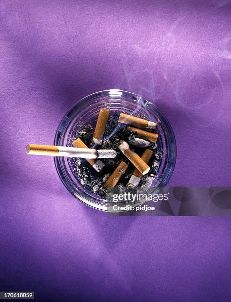 ashtray full with butts and burning cigarette - ashtray stock pictures, royalty-free photos & images
