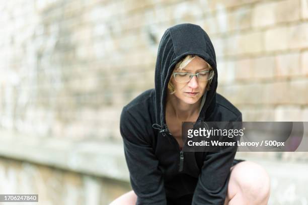 portrait of woman wearing hooded shirt sitting on steps getting ready for run,brussel,belgium - positivism stockfoto's en -beelden