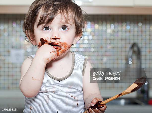 a little baby eating a cake while holding a wooden spoon - chocolate cake stockfoto's en -beelden