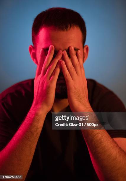close-up of man covering face with hands under red and blue lights,mental health issues and concepts - handen voor de ogen stockfoto's en -beelden