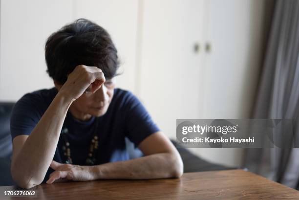 an elderly woman sits on a sofa and is distressed. - sighing stock pictures, royalty-free photos & images