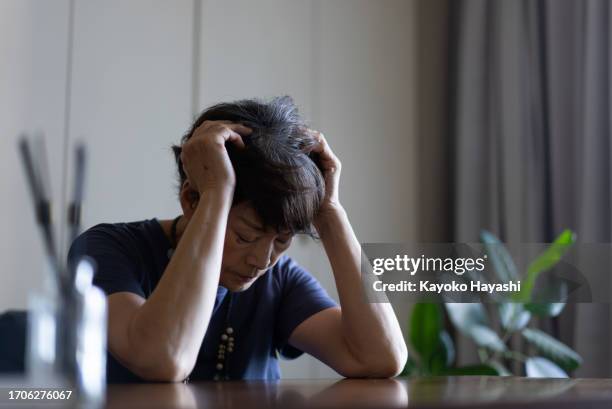 an elderly woman sits on a sofa and is distressed. - sighing stock pictures, royalty-free photos & images