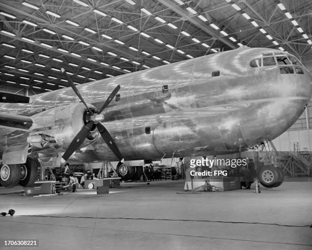 Technicians and engineers beneath the fuselage of a Boeing C-97 Stratofreighter, a four-engine, long-range heavy military cargo transport, as it is...