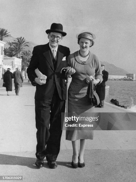 American-born British poet, playwright, writer, and publisher TS Eliot and his wife, Valerie Eliot, holding hands as they walk on the seafront while...