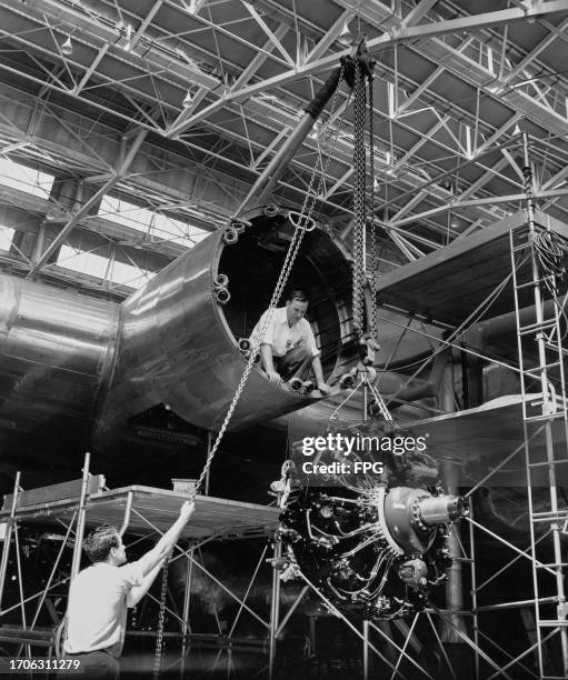 Two engineers hoist one of four Wright R-3350 Duplex-Cyclone engines into position during construction of a Boeing B-29 Superfortress heavy bomber at...
