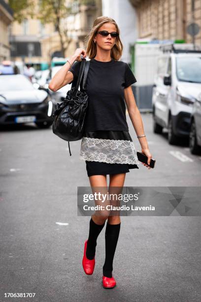 Guest wears a black t-shirt, black mini skirt with white lace details, black socks, red flat shoes and black bag, outside Marni, during the...