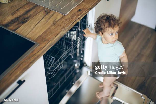 baby toddler is standing on an open dishwasher with dirty dishes inside - imperfection stock pictures, royalty-free photos & images