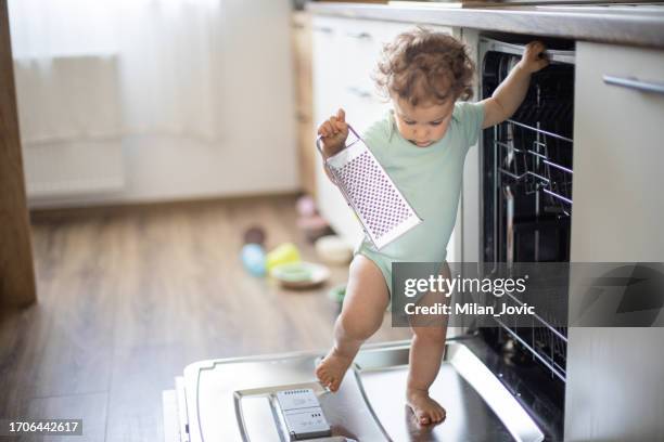 baby toddler is standing on an open dishwasher with dirty dishes inside - baby gate imagens e fotografias de stock