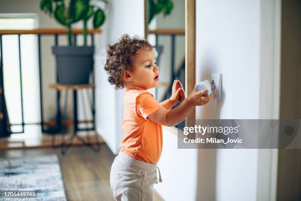el bebé alcanza la toma de corriente en la pared de la casa con la mano. - toma eléctrica fotografías e imágenes de stock