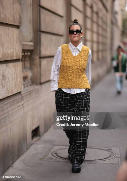 Louise Chen is seen wearing black sunglasses with golden logo detail from Miu Miu, silver heard-shaped earrings, a yellow knitted sweater vest,...