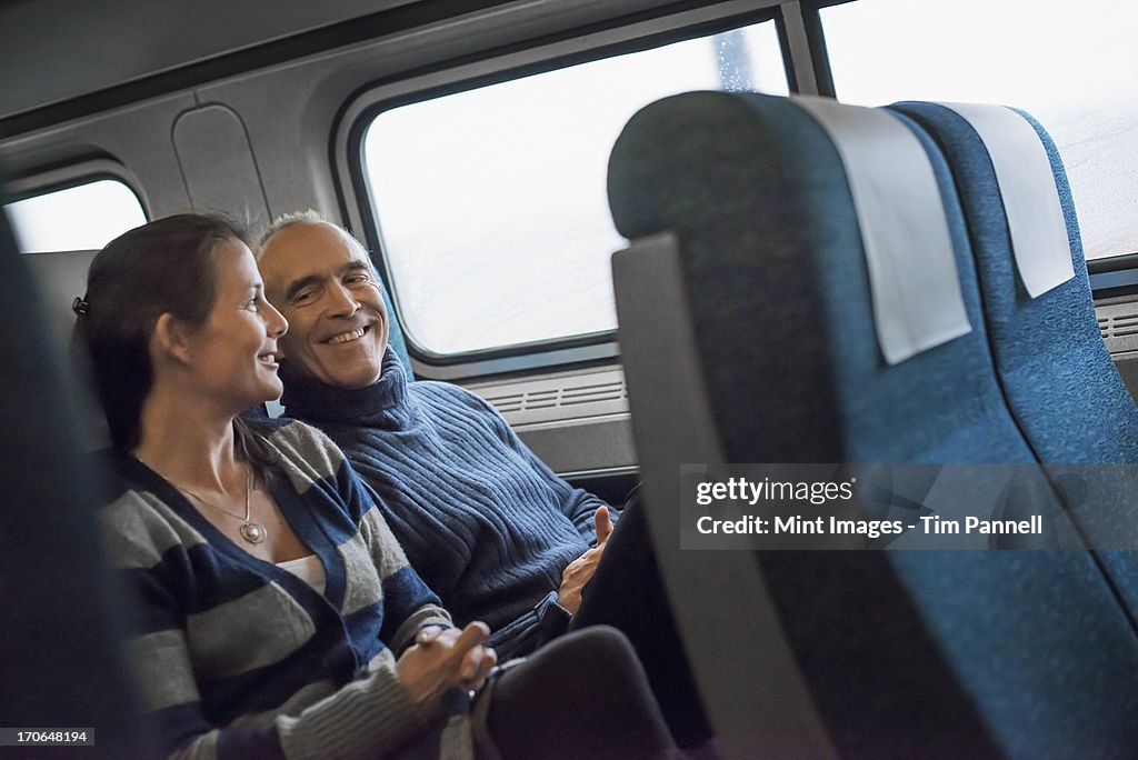 Two people sitting in a railway carriage, smiling. Taking a train journey.