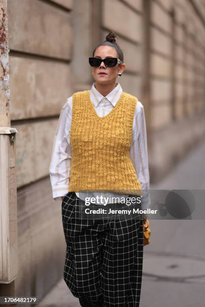 Louise Chen is seen wearing black sunglasses with golden logo detail from Miu Miu, silver heard-shaped earrings, a yellow knitted sweater vest,...