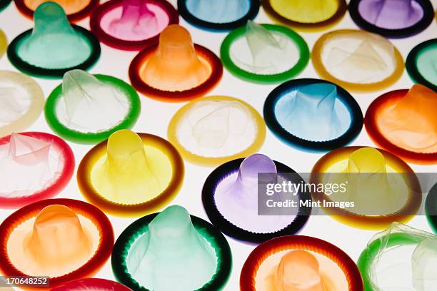 a large group of multi-colored condoms displayed on a white background. laid out neatly. - condoms - fotografias e filmes do acervo