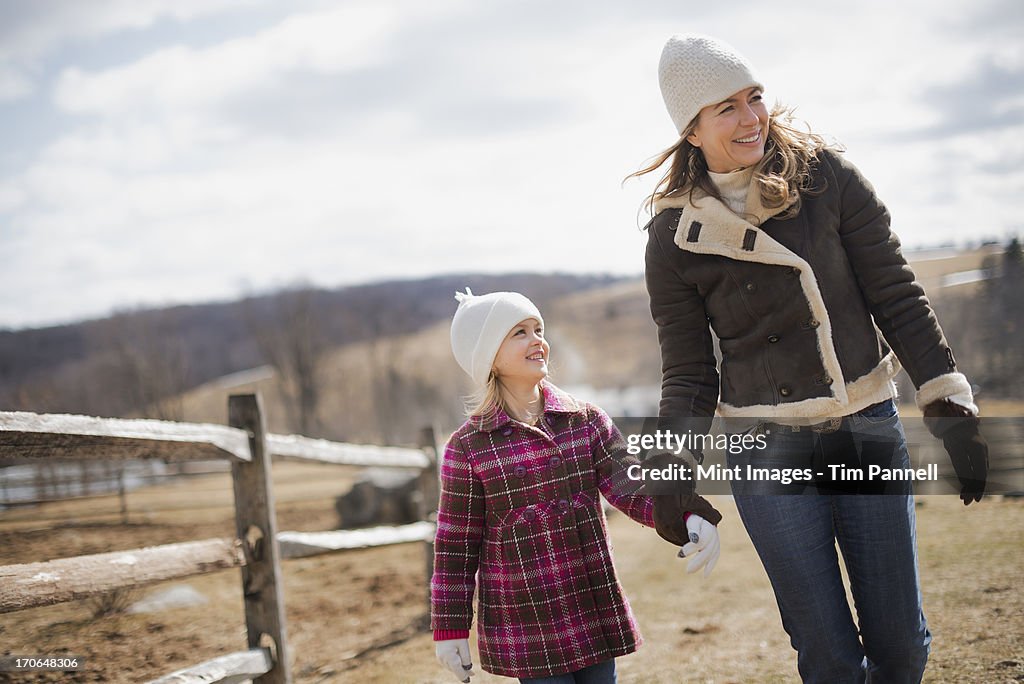 A woman and child walking along a path hand in hand on a farm in spring weather.