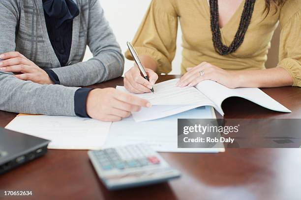 businesswoman watching woman sign paperwork - expectations business stock pictures, royalty-free photos & images