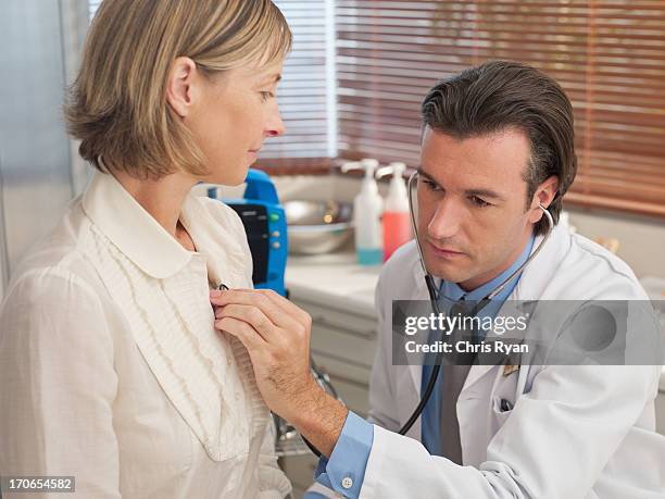 médecin écoute de patient 's battement de coeur dans la salle d'examen - blouse dexamen médical photos et images de collection