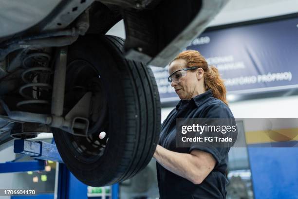 mujer mecánica de automóviles cambiando la rueda del automóvil en un taller de reparación - estereotipo-de-géneros fotografías e imágenes de stock