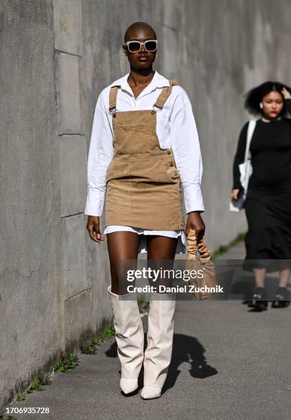 Guest is seen wearing a white shirt dress, tan overalls, tan bag and cream boots with cream sunglasses outside the Givenchy show during the...
