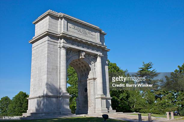 stone arched monument amid trees under blue skies - valley forge stockfoto's en -beelden