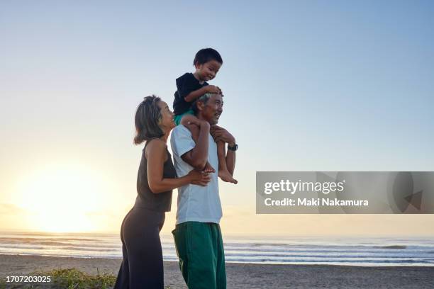 father carrying an infant on his shoulders on the shore at sunrise, and a mother beside him. - east asia stock pictures, royalty-free photos & images