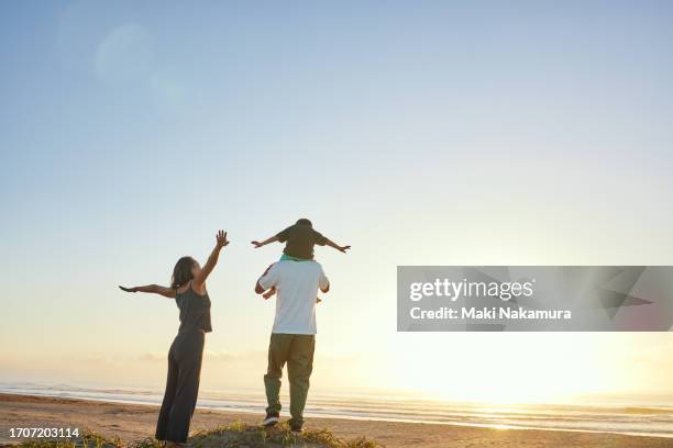 father carrying an infant on his shoulders on the shore at sunrise, and a mother beside him. - famiglia con figlio unico foto e immagini stock