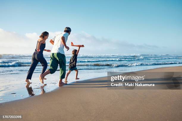 parents running behind a boy running straight ahead with a model airplane held high in one hand. - familia fotografías e imágenes de stock