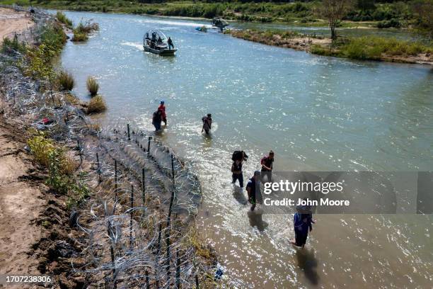 Immigrants walk along the fortified bank of the Rio Grande after crossing the border from Mexico into the United States as U.S. Border Patrol agents...