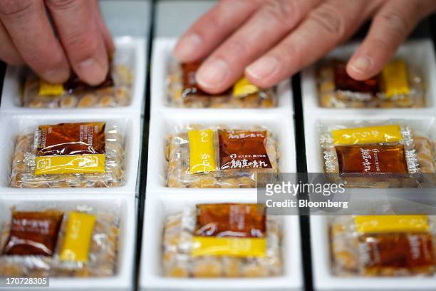 An employee aligns sachets of seasoning sauce and mustard on top of polystyrene trays of fermented soybeans, known as natto, as they move along a...