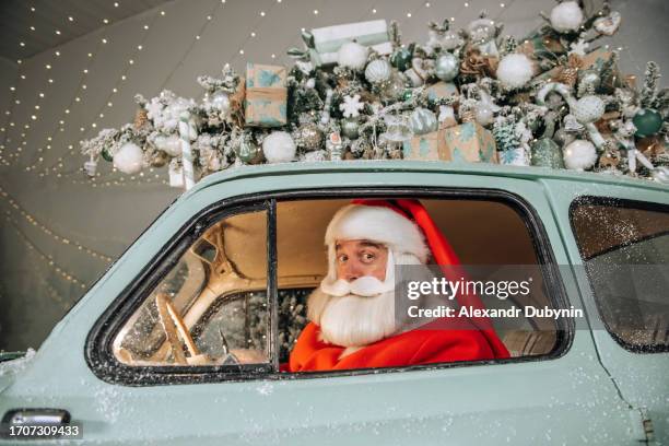 portrait of santa claus sitting behind the wheel of a car delivering his gifts and a christmas tree. christmas delivery concept - christmas driving stock pictures, royalty-free photos & images