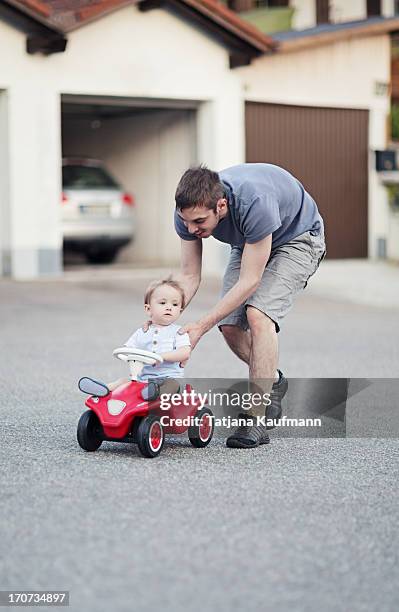 baby on toy car being pushed by daddy - bobbycar stockfoto's en -beelden