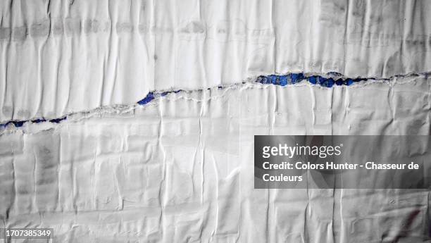 posters in wrinkled white paper, pasted and torn on a blue wall (visible in the tear) in paris, france - couleurs fond stock-fotos und bilder