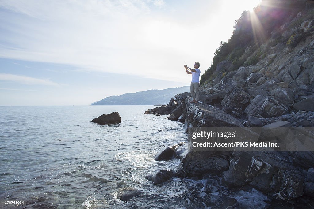 Man stands on rock above sea, takes picture