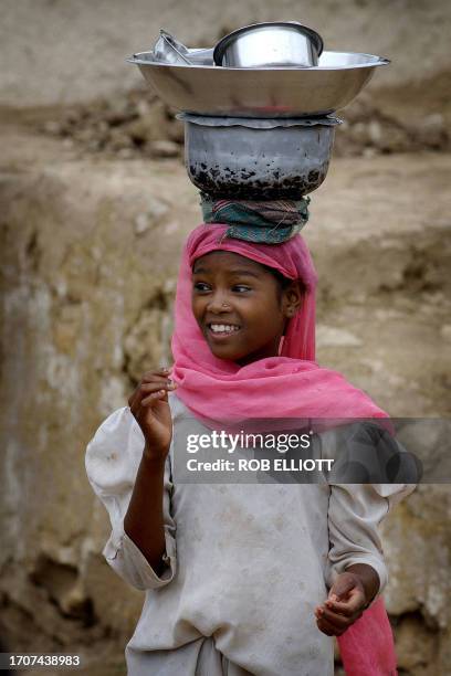 Sidhi girl dressed in colourful veil carries dishes on top of her head as she walks through Zambur village outside Junagadh city, in the state...