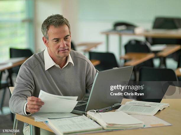 Professor Using Laptop With Reveiwing Paperwork In Classroom, 照片檔