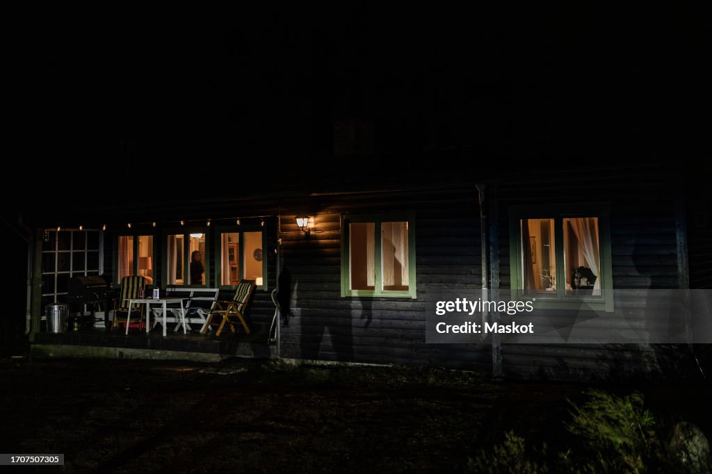 Shadow of demon on illuminated cabin at night